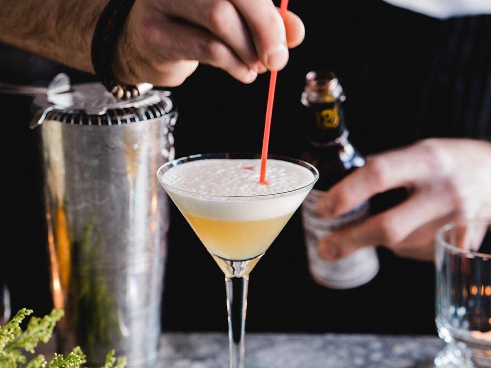 A bartender stirring a cocktail beside a shaker