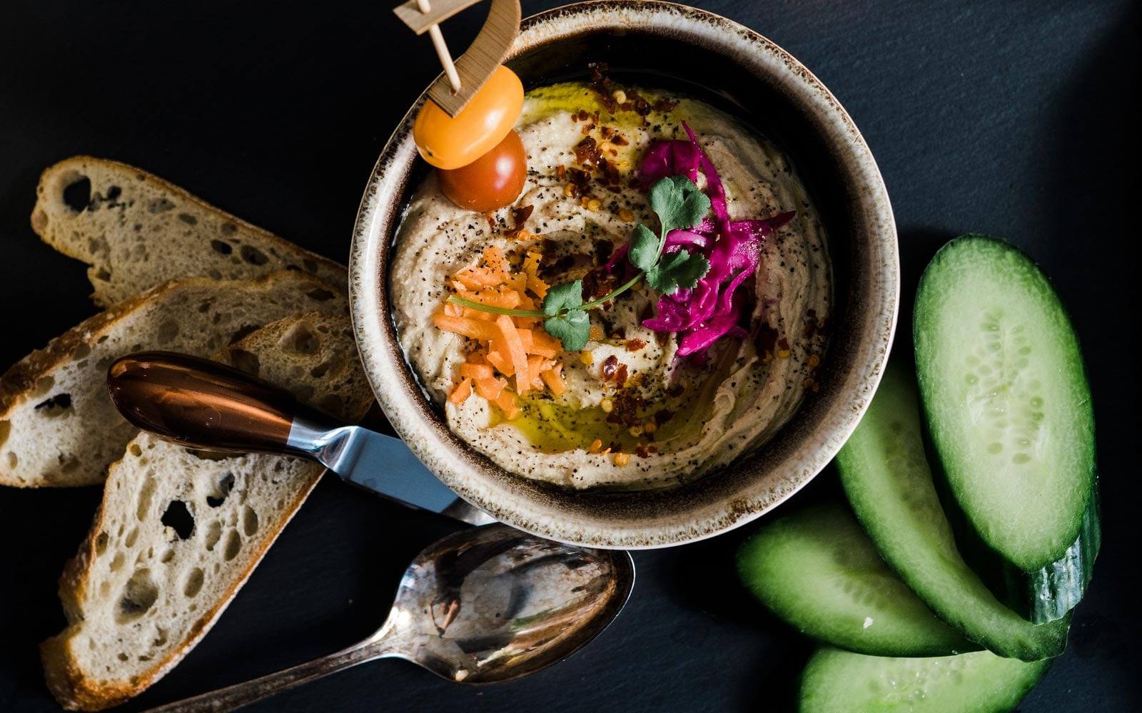 A bowl of hummus with bread and cucumber